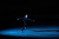 Professional figure skating artist slides and spins on the ice in the arena in the rays of blue light. Young woman