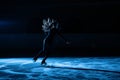 Professional figure skating artist slides and spins on the ice in the arena in the rays of blue light. Young woman