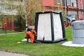 A professional firefighter in an orange special fireproof suit prepares to assemble a white oxygen tent to rescue people at a chem