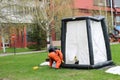 A professional firefighter in an orange special fireproof suit prepares to assemble a white oxygen tent to rescue people at a chem