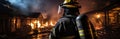 A professional firefighter puts out the flames. A burning house and a man in uniform, view from the back.