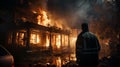 A professional firefighter puts out the flames. A burning house and a man in uniform, view from the back.