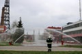 Professional firefighters in orange fire-resistant suits in white helmets with gas masks are testing fire hoses and fire guns to e