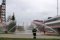 Professional firefighters in orange fire-resistant suits in white helmets with gas masks are testing fire hoses and fire guns to e