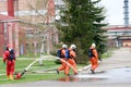 Professional firefighters in orange fire-resistant suits in white helmets with gas masks are testing fire hoses and fire guns to e