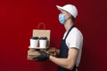 Professional food delivery man in a protective mask and gloves holds boxes of pizza and coffee and gives the client, fast delivery