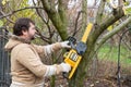 Professional gardener cuts branches on a tree, with using electric battery powered chain saw. Season pruning. Trimming trees with Royalty Free Stock Photo