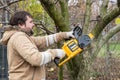 Professional gardener cuts branches on a tree, with using electric chain saw. Season pruning. Trimming trees with chainsaw in Royalty Free Stock Photo