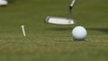 Professional golfer putting ball into the hole. Golf ball by the edge of hole with player in background on a sunny day Royalty Free Stock Photo