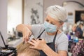 Professional hairdresser with face mask cut hair with scissors and comb. A boy gets a trendy haircut. Barber services with Royalty Free Stock Photo