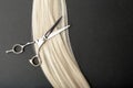 Professional hairdresser scissors with long strand of blonde hair on black background. Flat lay composition with Hairdresser tools
