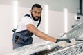 Professional handsome dark skinned man worker washing a soapy car hood with a beige sponge, posing and looking at camera Royalty Free Stock Photo