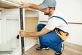 Professional handyman, male worker in uniform using spirit level while checking measurements of kitchen cabinet indoors Royalty Free Stock Photo