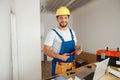 Professional handyman worker in uniform wearing tool belt and hardhat smiling at camera, holding hammer during Royalty Free Stock Photo