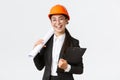 Professional happy asian female architect, construction engineer in helmet and business suit holding blueprints and Royalty Free Stock Photo