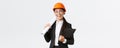 Professional happy asian female architect, construction engineer in helmet and business suit holding blueprints and Royalty Free Stock Photo