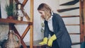 Professional housekeeper is dusting furniture with wet cloth, woman is wearing protective gloves, casual clothing and