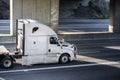 Professional industrial grade white big rig semi truck with flat bed semi trailer running on the road under the bridge Royalty Free Stock Photo