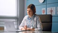 Professional lady doctor conducts online checkup talking to patient and looking at grey laptop display