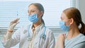 Professional lady general practitioner injects young woman patient in blue disposable face mask