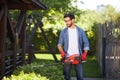 Professional landscaper cutting, pruning evergreen conifer bush with hedge trimmer in park.