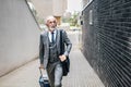 Professional with laptop bag and suitcase looking away while walking by the business offices building Royalty Free Stock Photo