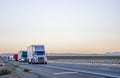 Professional long haul big rigs semi truck transporting cargo in semi trailers running on the straight highway road at twilight Royalty Free Stock Photo