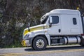 Professional low cab profile big rig white semi truck tractor with oversize load sign on the bumper running on the mountain road