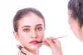 Make-up artist holding brush in her hand while applying some lipstick on young woman pretty face on white background Royalty Free Stock Photo