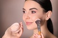 Professional makeup artist applying powder onto beautiful young woman`s face with brush on dusty rose background, closeup Royalty Free Stock Photo