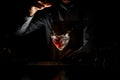 Professional male bartender throwing a big red rose bud to a martini glass with a cocktail in the dark Royalty Free Stock Photo