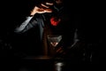 Professional male bartender throwing a red rose bud to a martini glass with a cocktail in the dark Royalty Free Stock Photo