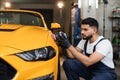 Professional male car service worker holding in hands orbital polisher, and polishing yellow car Royalty Free Stock Photo