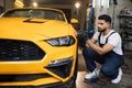 Professional male car service worker holding in hands orbital polisher, and polishing yellow car Royalty Free Stock Photo