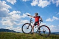 Professional male cyclist in sportswear and helmet standing with cross country bike on top of hill Royalty Free Stock Photo