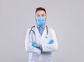 Professional male doctor in uniform, face mask and rubber gloves posing over grey studio background Royalty Free Stock Photo