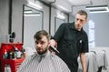 Professional male hairdresser does hairstyle to bearded man in barber shop, client looks into camera with serious face. Barber Royalty Free Stock Photo