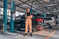 A professional male mechanical employee of a car service workshop stand with crossed arms and tools, looks very symphaticly and
