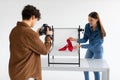 Professional male photographer and female assistant doing content photoshoot for shoes, working in team in photostudio