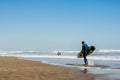 Professional male surfer carrying his surfboard while walking along a sand beach Royalty Free Stock Photo