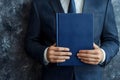 Professional Man in Dark Suit Holding a Blue Bound Document with Textured Background Royalty Free Stock Photo