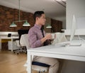 Professional man in office drinking coffee while working on desktop computer Royalty Free Stock Photo
