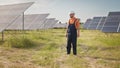 Professional man technician in hard hat walks on new ecological solar construction outdoors. Farm of solar panels