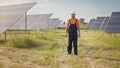 Professional man technician in hard hat walks on new ecological solar construction outdoors. Farm of solar panels