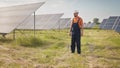 Professional man technician in hard hat walks on new ecological solar construction outdoors. Farm of solar panels