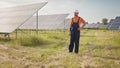 Professional man technician in hard hat walks on new ecological solar construction outdoors. Farm of solar panels