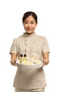 Professional masseuse in uniform holding tray with spa supplies on white