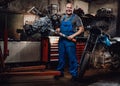 Professional mechanic stands next to the suspended flat engine and naked bike in garage