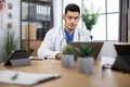 Professional young Arab medical specialist using laptop at work in modern clinic