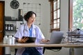 Professional Asian female doctor using laptop, checking medical record on medical clipboard Royalty Free Stock Photo